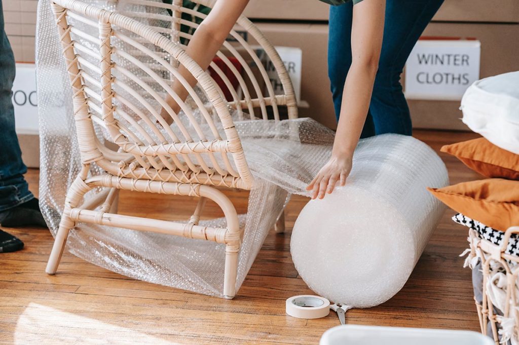 Persons wrapping a chair in bubble wrap