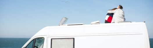 A couple sitting on top of their stationary caravan, looking out to sea.