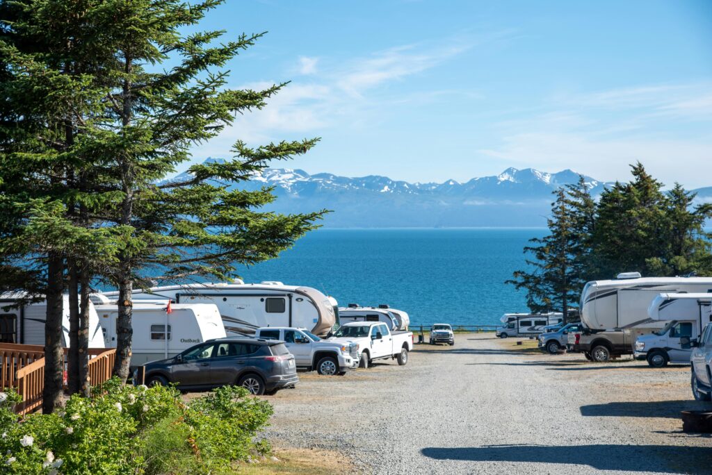 Caravans parked outside a large lake, in front of an alpine mountain range.